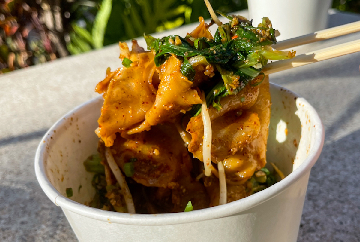 chopsticks hold up thick biangbiang noodles coated in spicy Szechuan sauce and garnished with fresh scallions