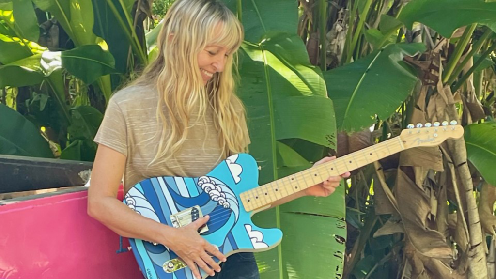 Heather Brown holding a guitar featuring her artwork of a wave